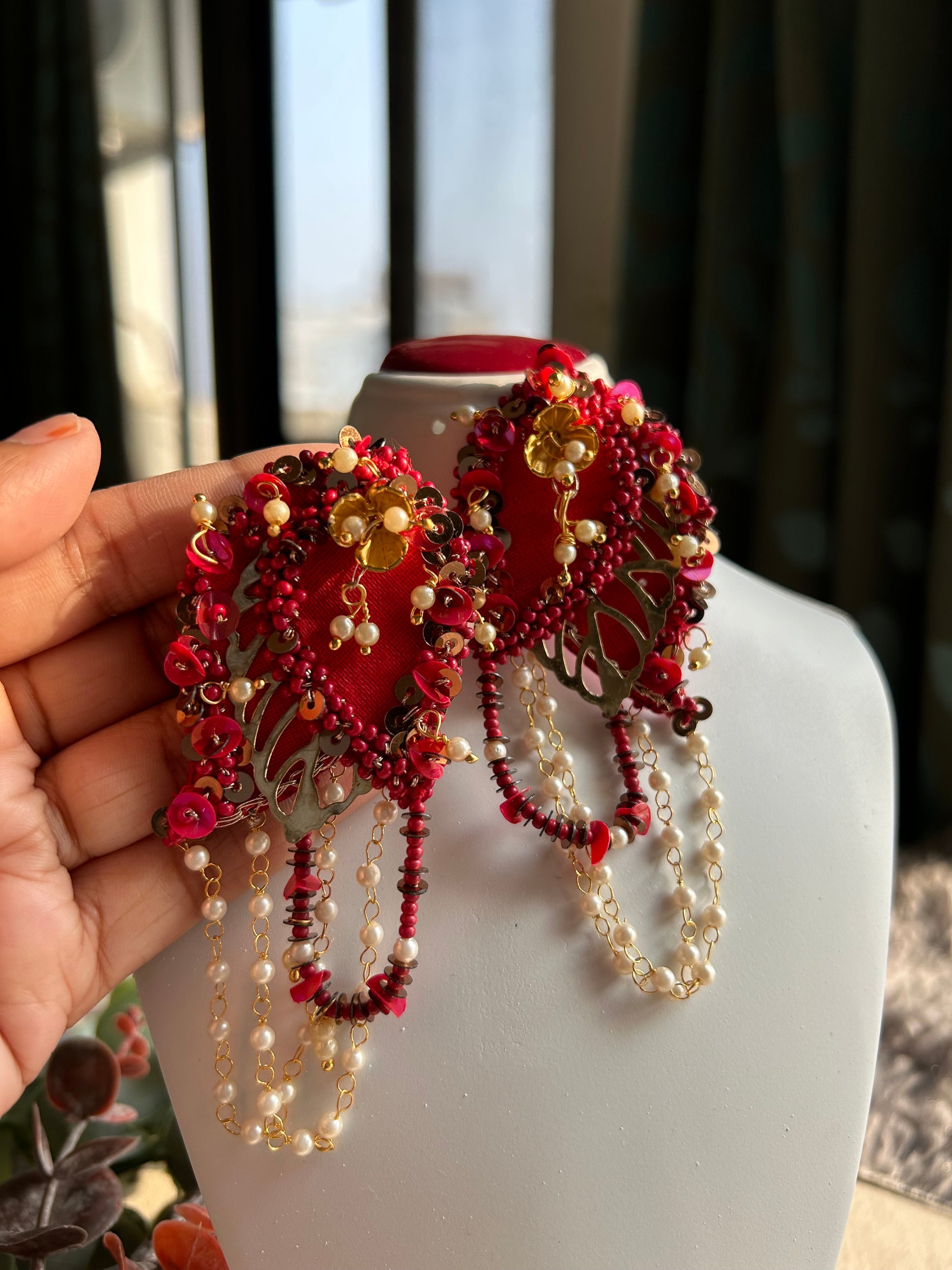 Close-up of handcrafted red embroidered earrings showing intricate beadwork and gold-toned leaf cutwork detail